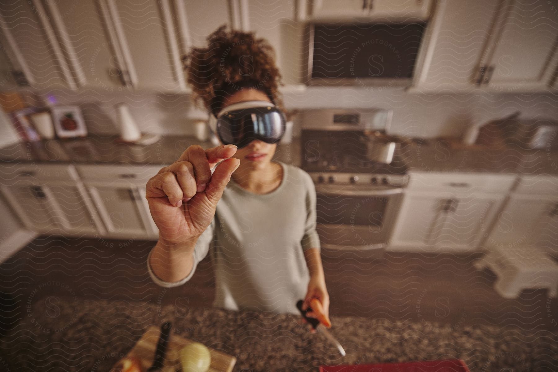 Woman standing in the kitchen holding tools with one hand and using virtual reality glasses