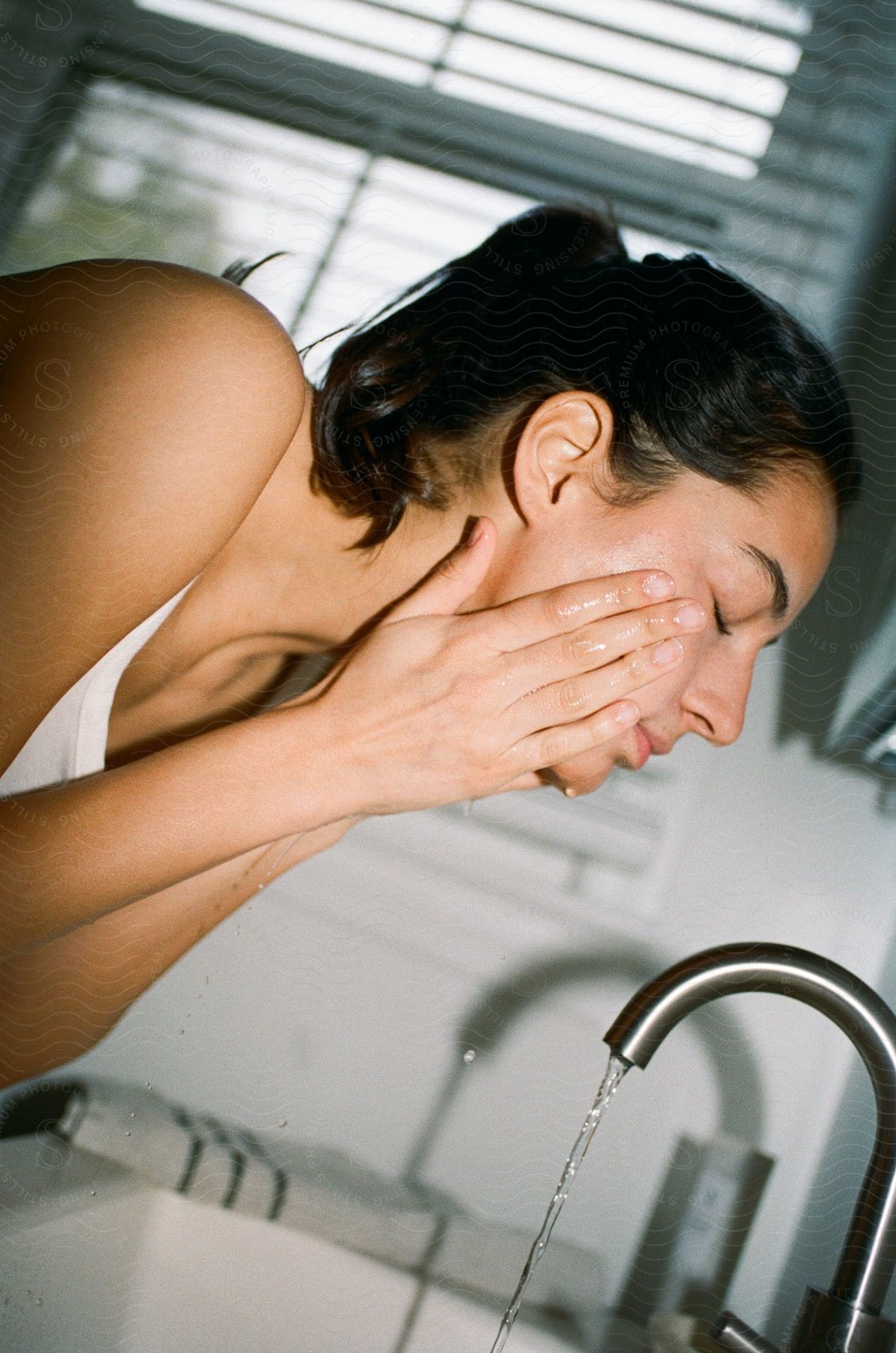 A Woman Washes Her Face Over A Running Sink