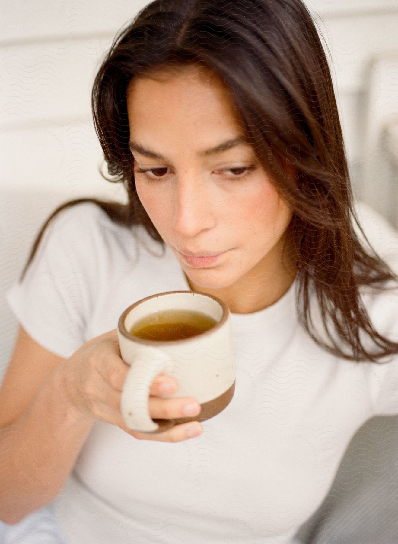 Woman with brown hair and a white shirt drinks a cup of tea