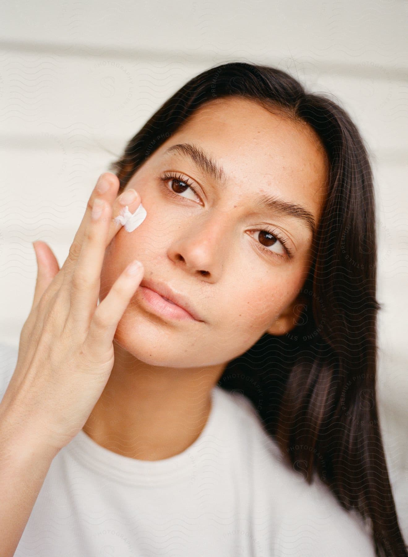 Woman is putting cream on her face with her finders