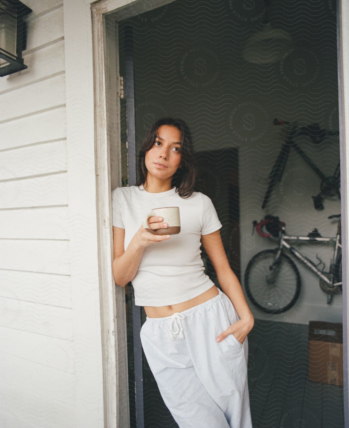 lady holds a coffee mug while leaning against the entrance door at mid-day