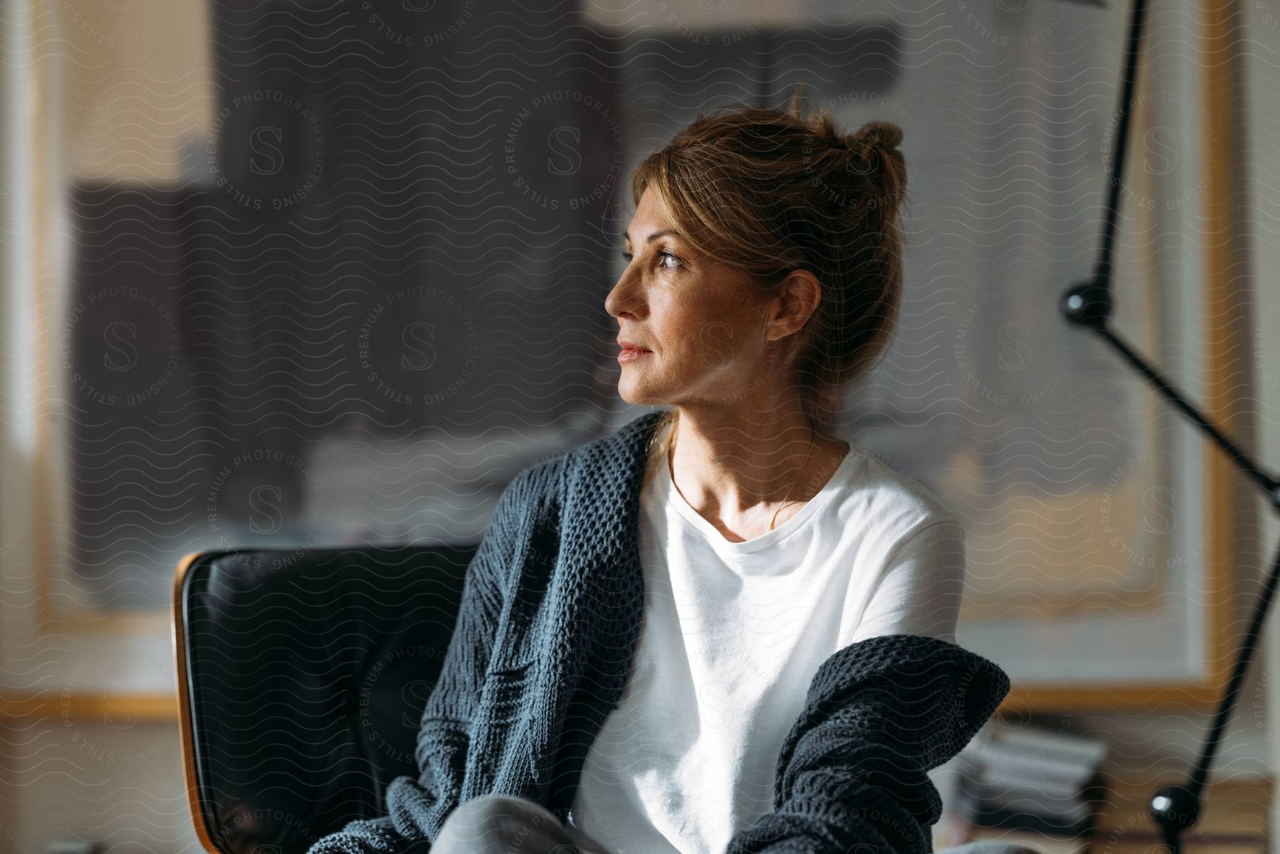 A woman posed sitting in profile next to a jointed lamp in front of a modern abstract painting