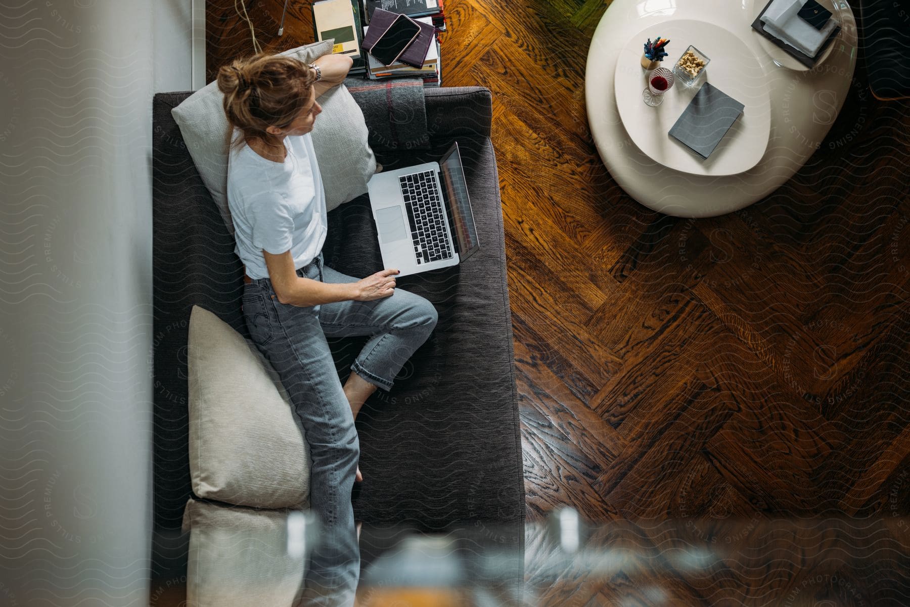 Stock photo of woman lying on gray sofa with her laptop in living room with laminate floor