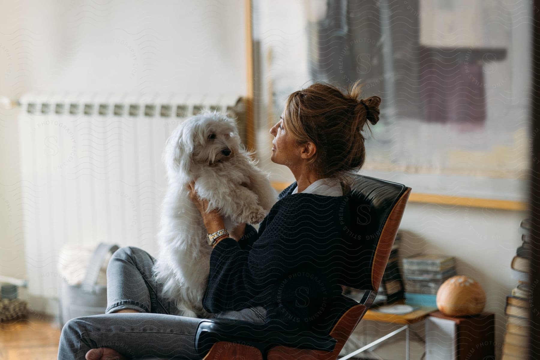 A woman in a living room cuddles a white dog on her lap.