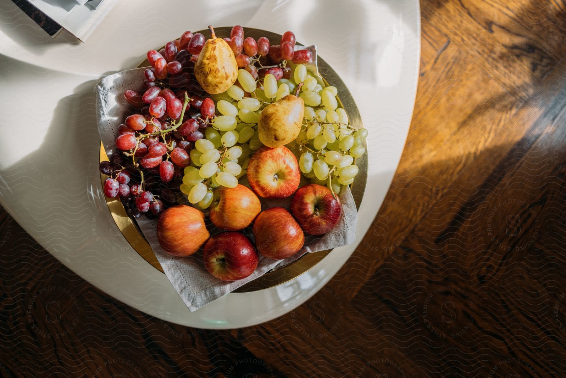 Grapes pears and apples on a gold colored plate on a wooden table with sunlight shining in