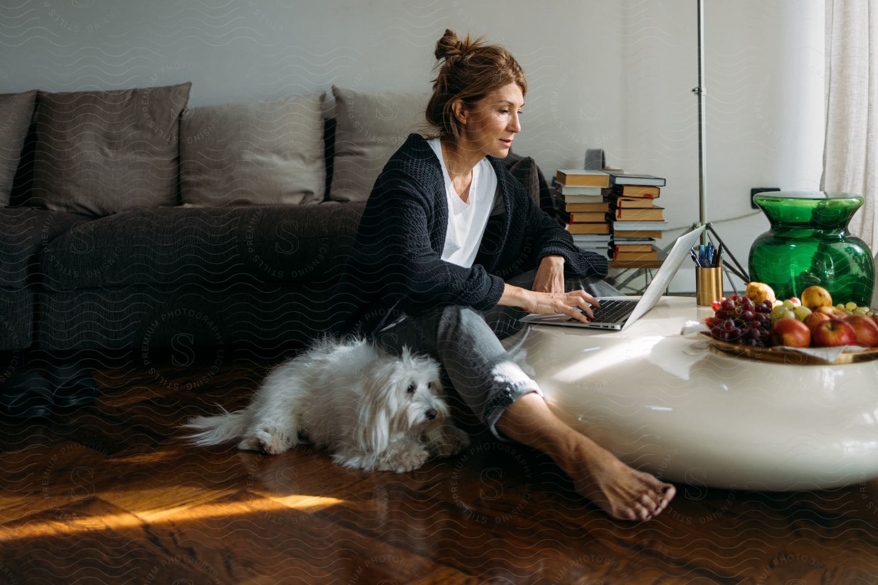 Woman sitting on her living room floor typing on a laptop computer as her dog lies next to her