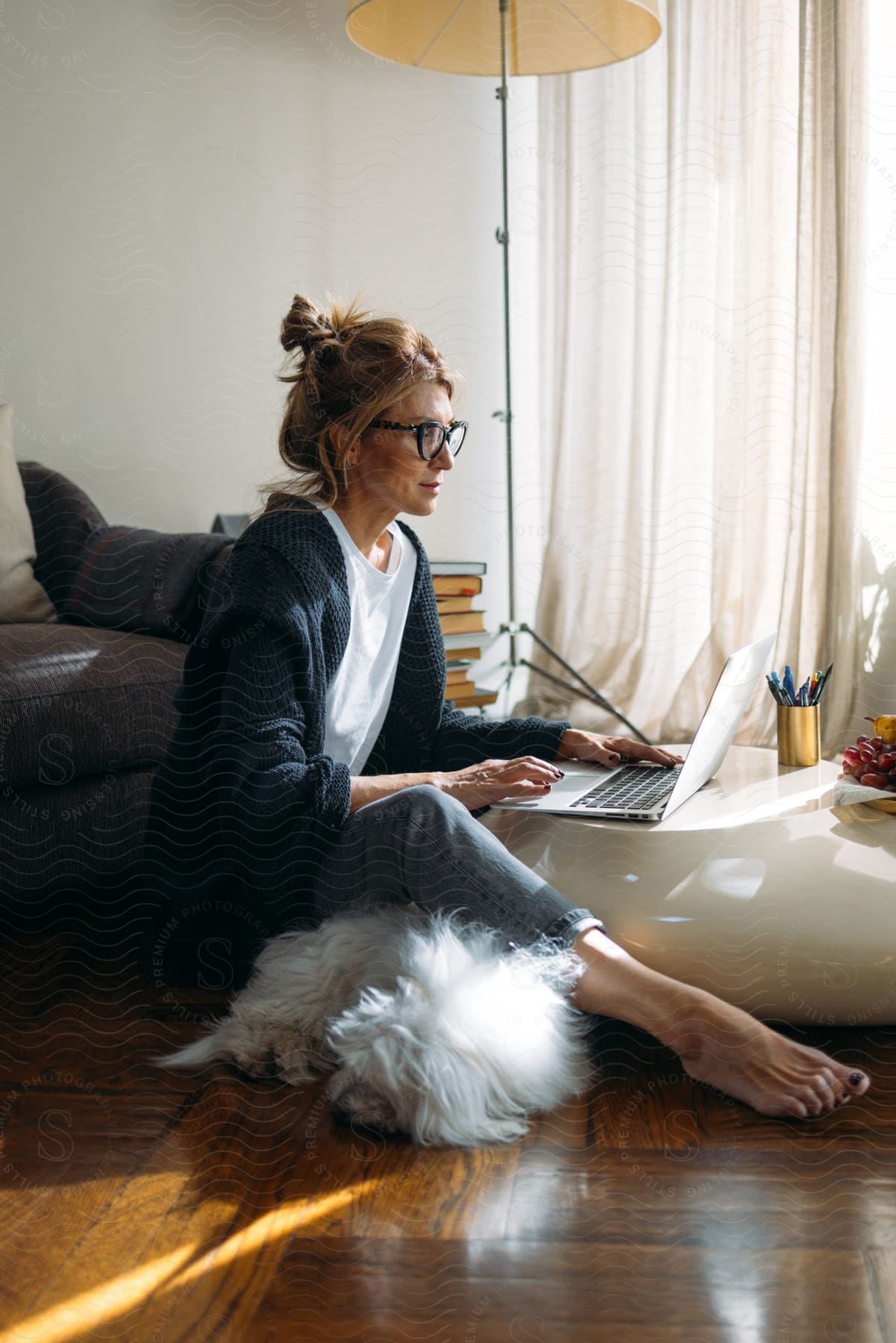 Woman sitting on her living room floor typing on a laptop computer as her dog lies next to her