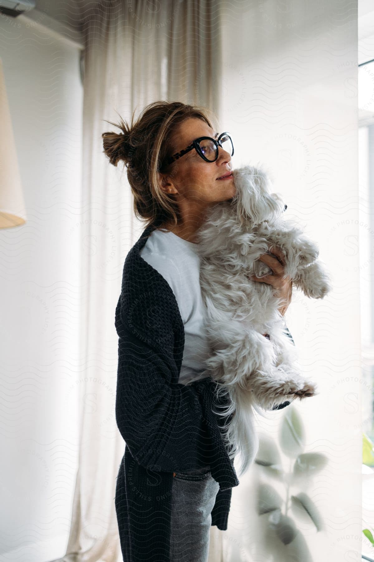Woman in glasses and black sweater holding a white dog indoors.