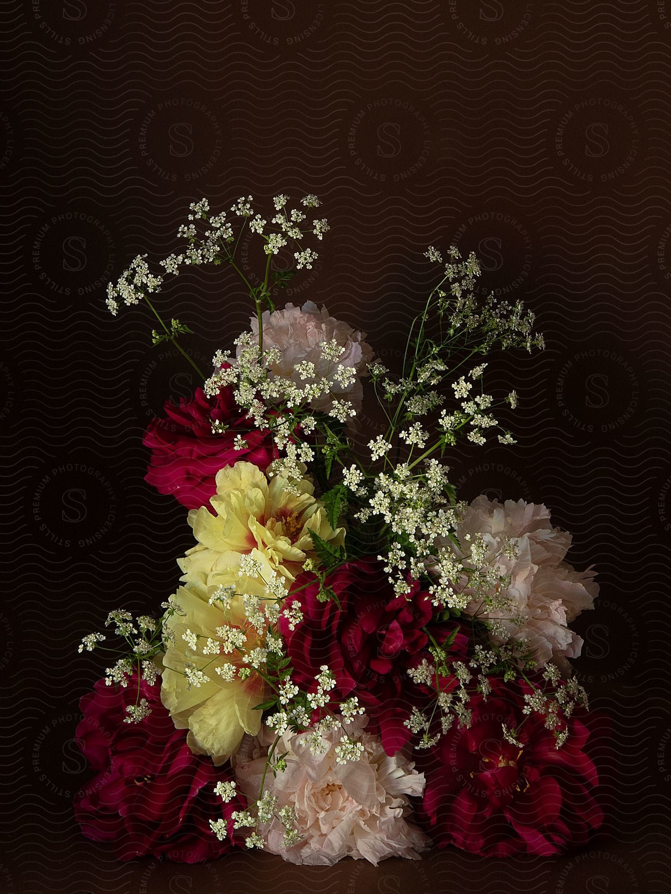 Still life of flowers of different colors with lilies and on a dark brown background