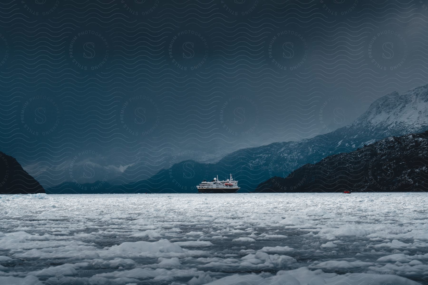 An ice-filled waterway with a cruise ship in the distance, mountains behind it, and dark clouds above.