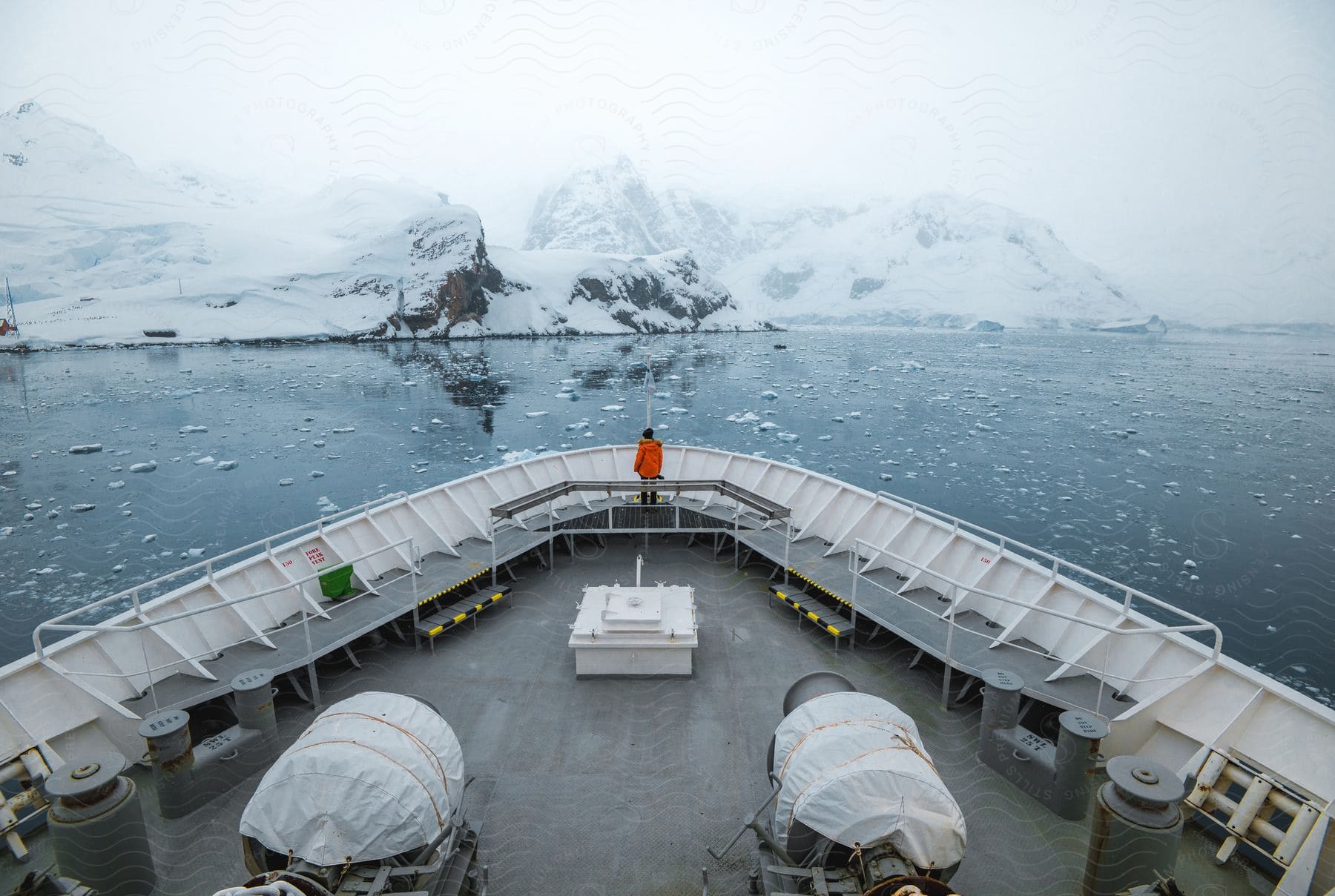 A person stands on the bow of a ship in an arctic ocean area.