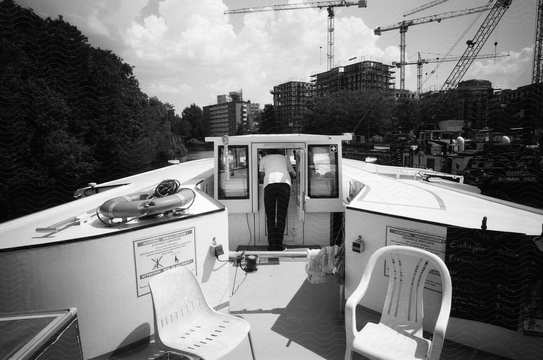 Cabin of a boat at the top with a view of a man from the back in a black and white image with a city being built around it