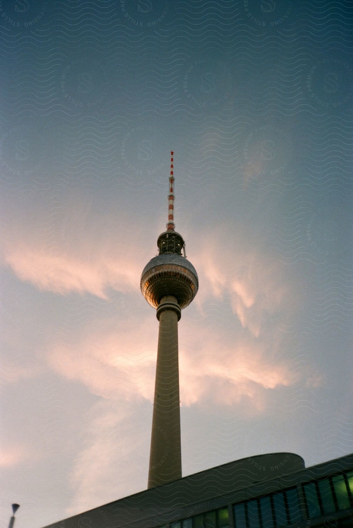 Berlin's TV tower pierces a cloudy sky above Alexanderplatz with a building nearby.