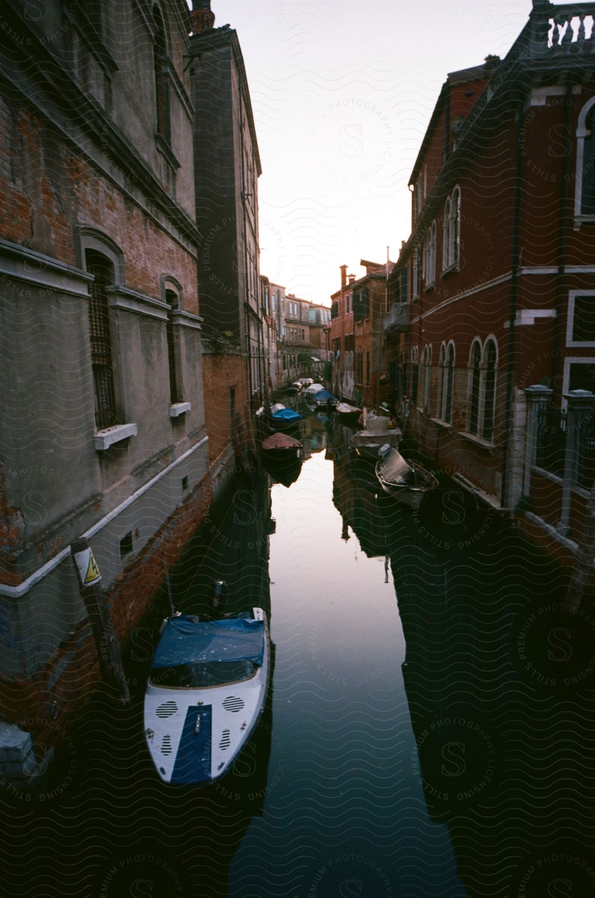 A tranquil canal is flanked by old, colorful buildings in the fading light of dusk, with boats gently moored along the sides.