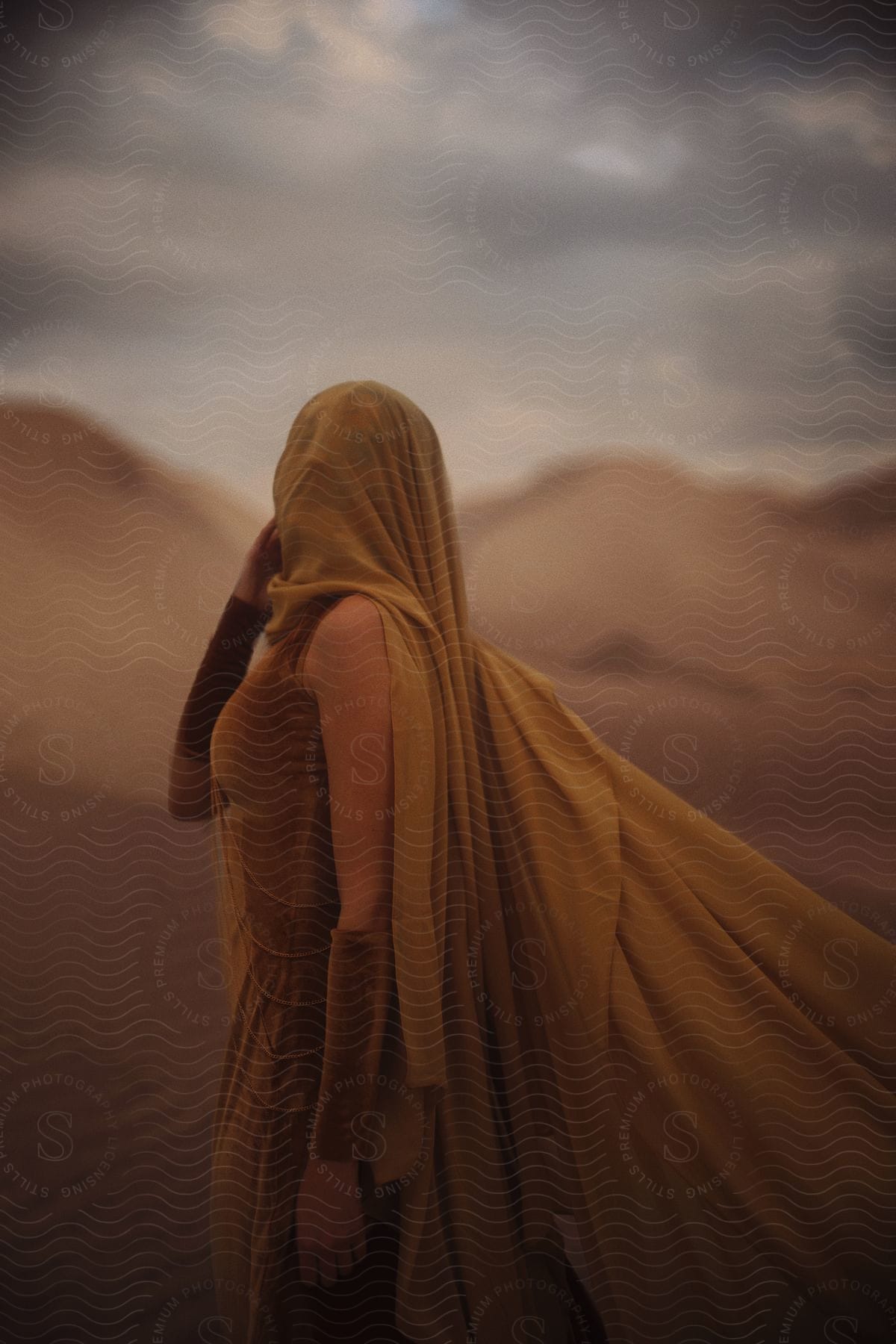 Woman With Her Head Covered Wearing A Long Gown Is Standing Among The Desert Dunes Under A Cloudy Sky