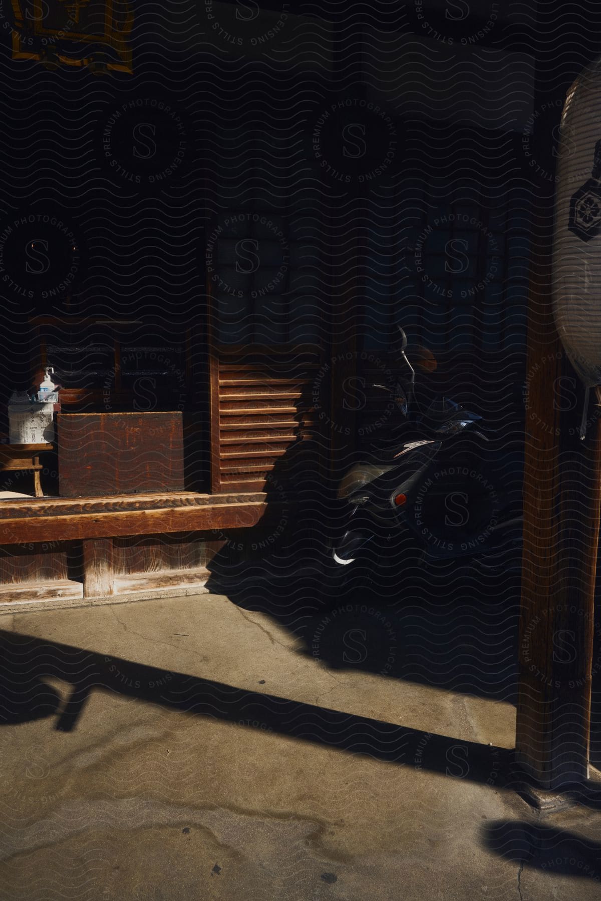 A scooter is parked in the shade against a wooden wall, illuminated by the natural light from the entrance. The atmosphere seems peaceful and serene.