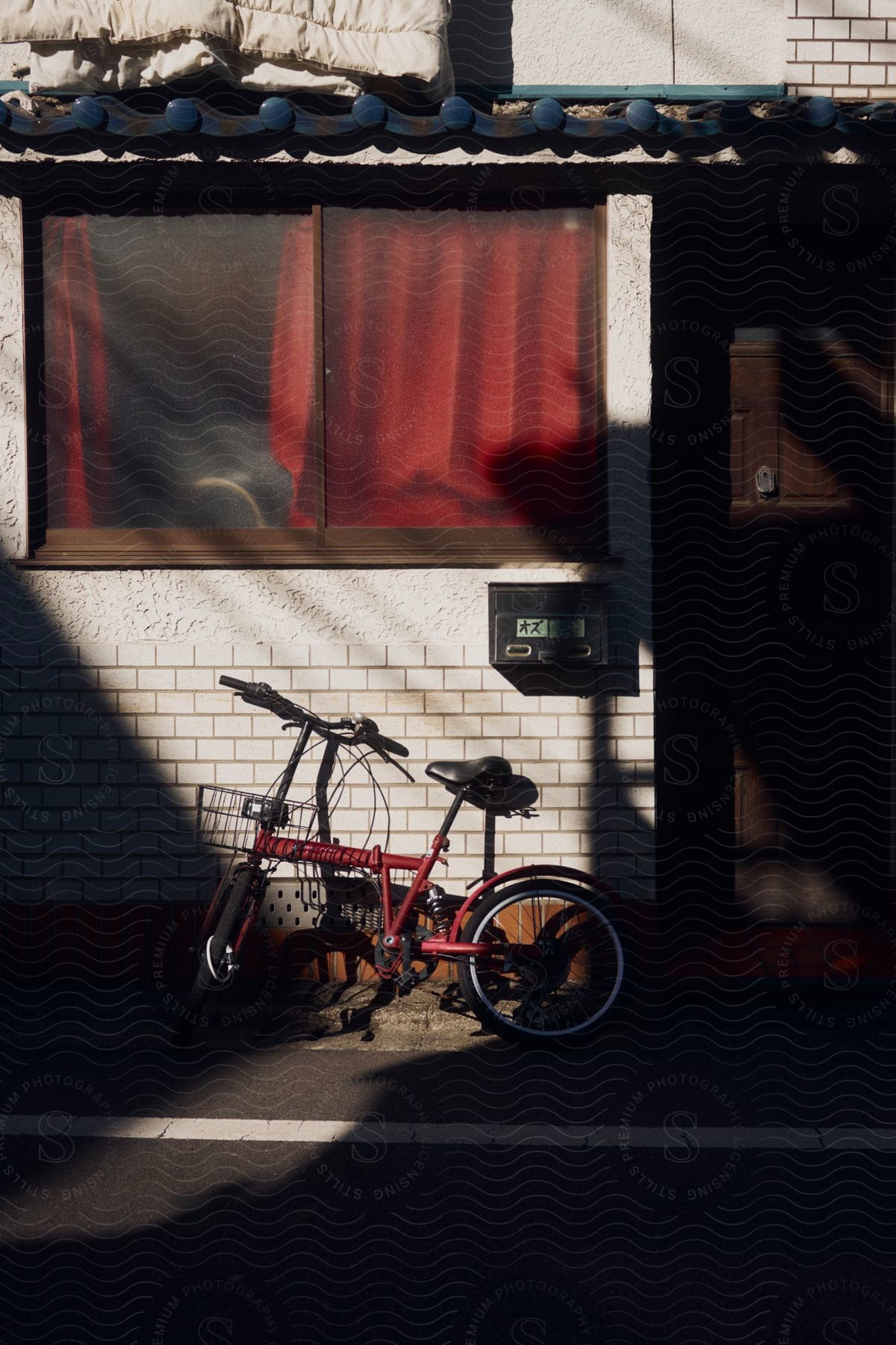 A red bicycle with a wire basket leaning against a white brick wall of an apartment home