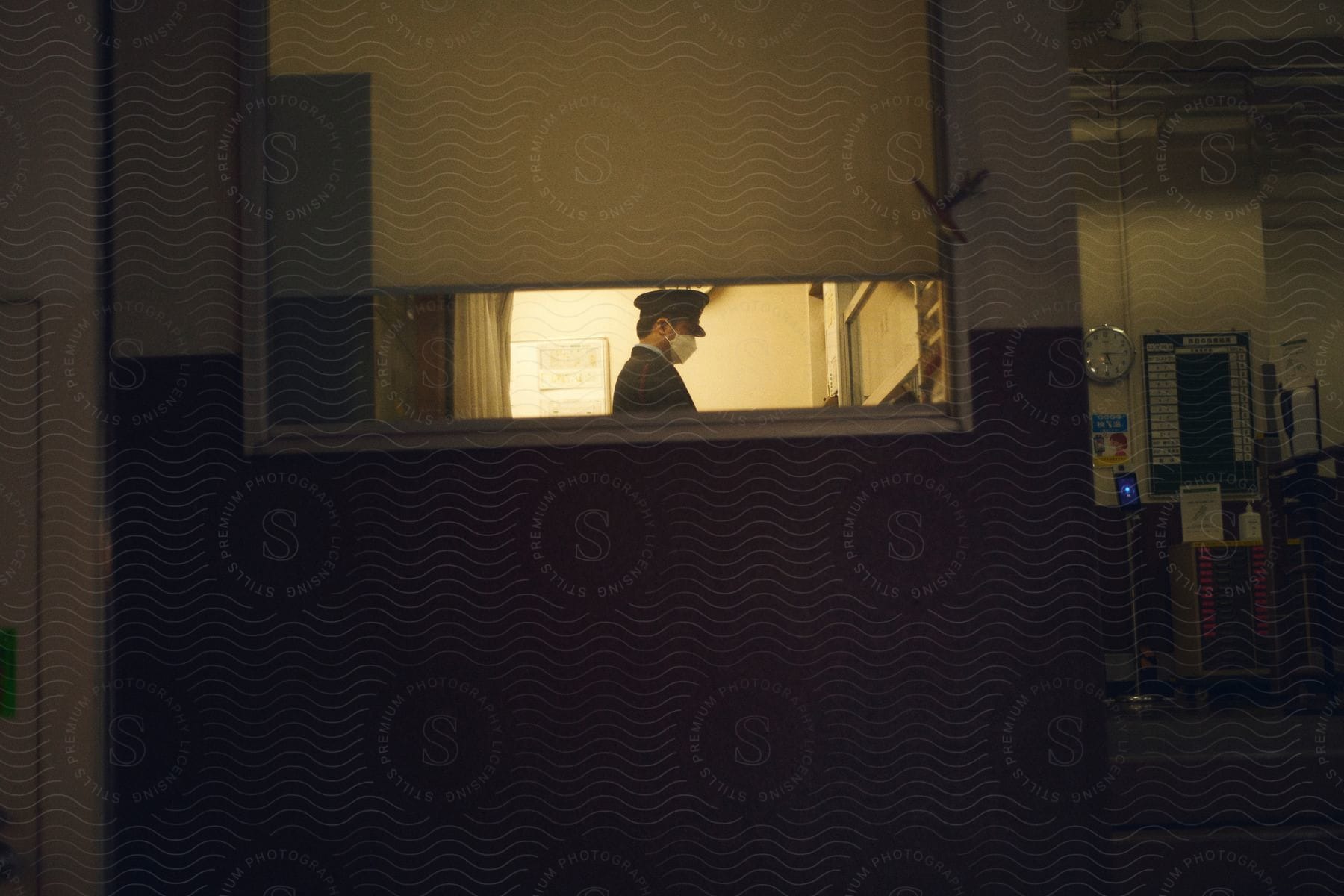 The face of a person wearing a beret and mask and is behind a lit window