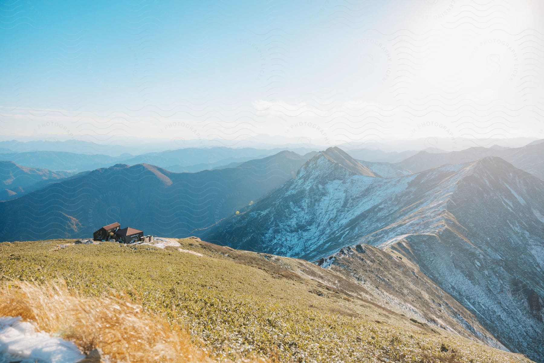 A serene landscape with a small cabin on a mountaintop, surrounded by majestic mountains under a bright sky.