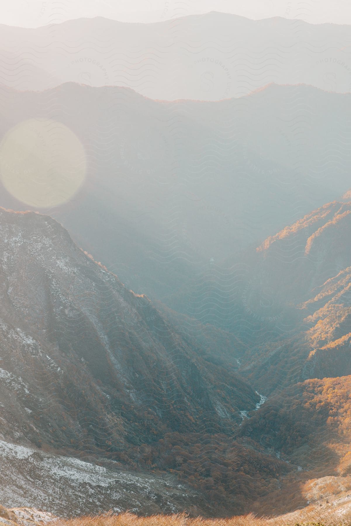 A valley with a river between several mountains and a great flair of sunlight across the sky