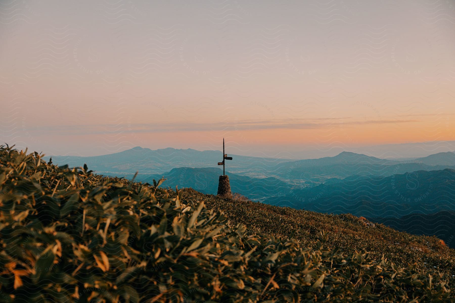 Cross monument on a hilltop at twilight with a view of distant mountains and a soft sky.