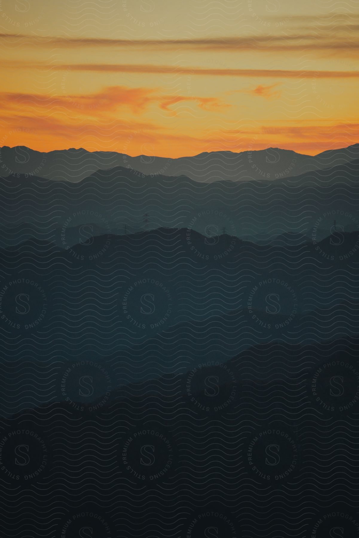 The sun sets in an orange sky over a mountain range.