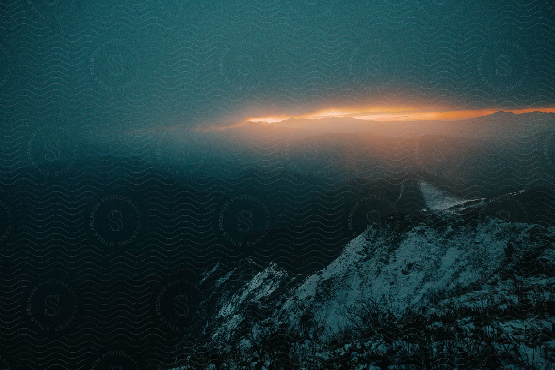 A view of a peak gave a mountain that is with snow and is the horizon at sunset with the orange sky