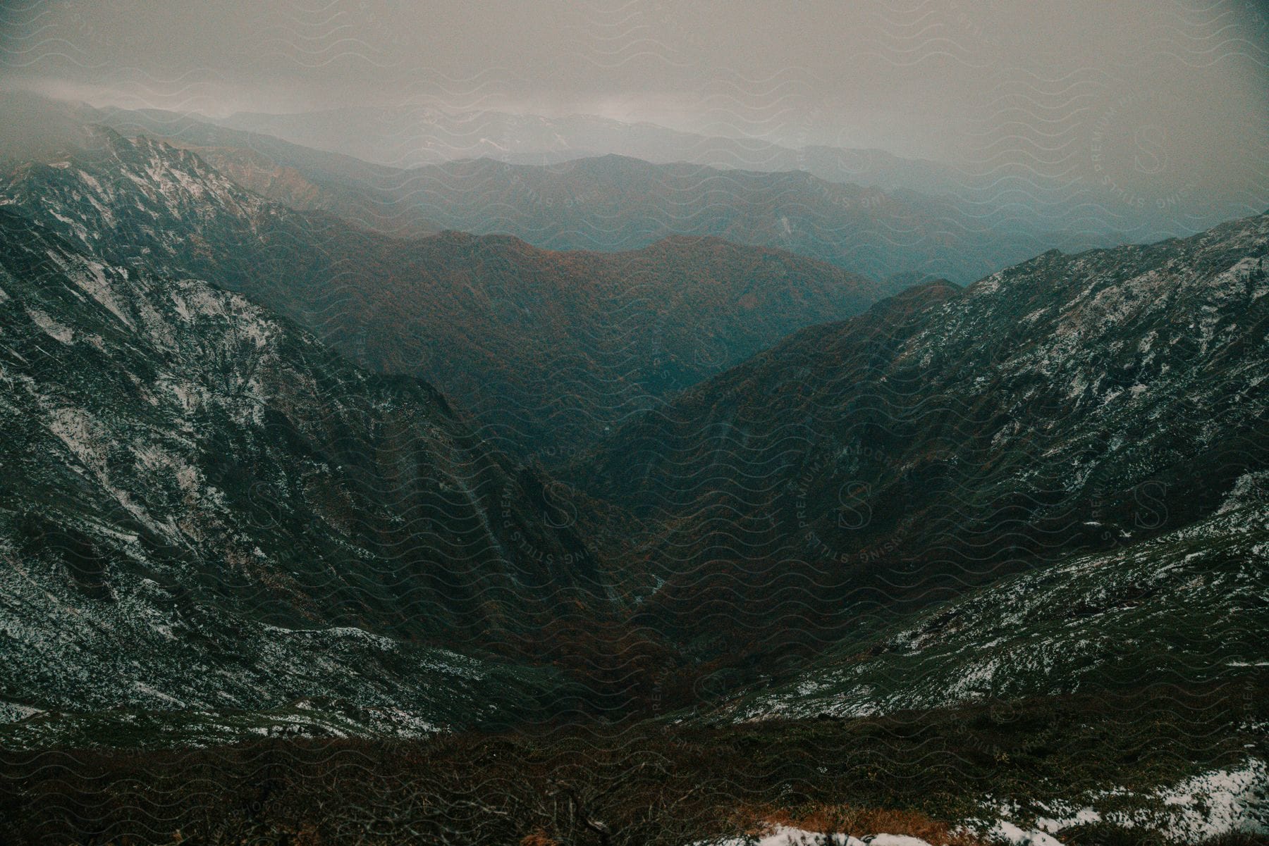 Snow On Mountain Slopes With Mountains In The Distance Under A Cloudy Sky