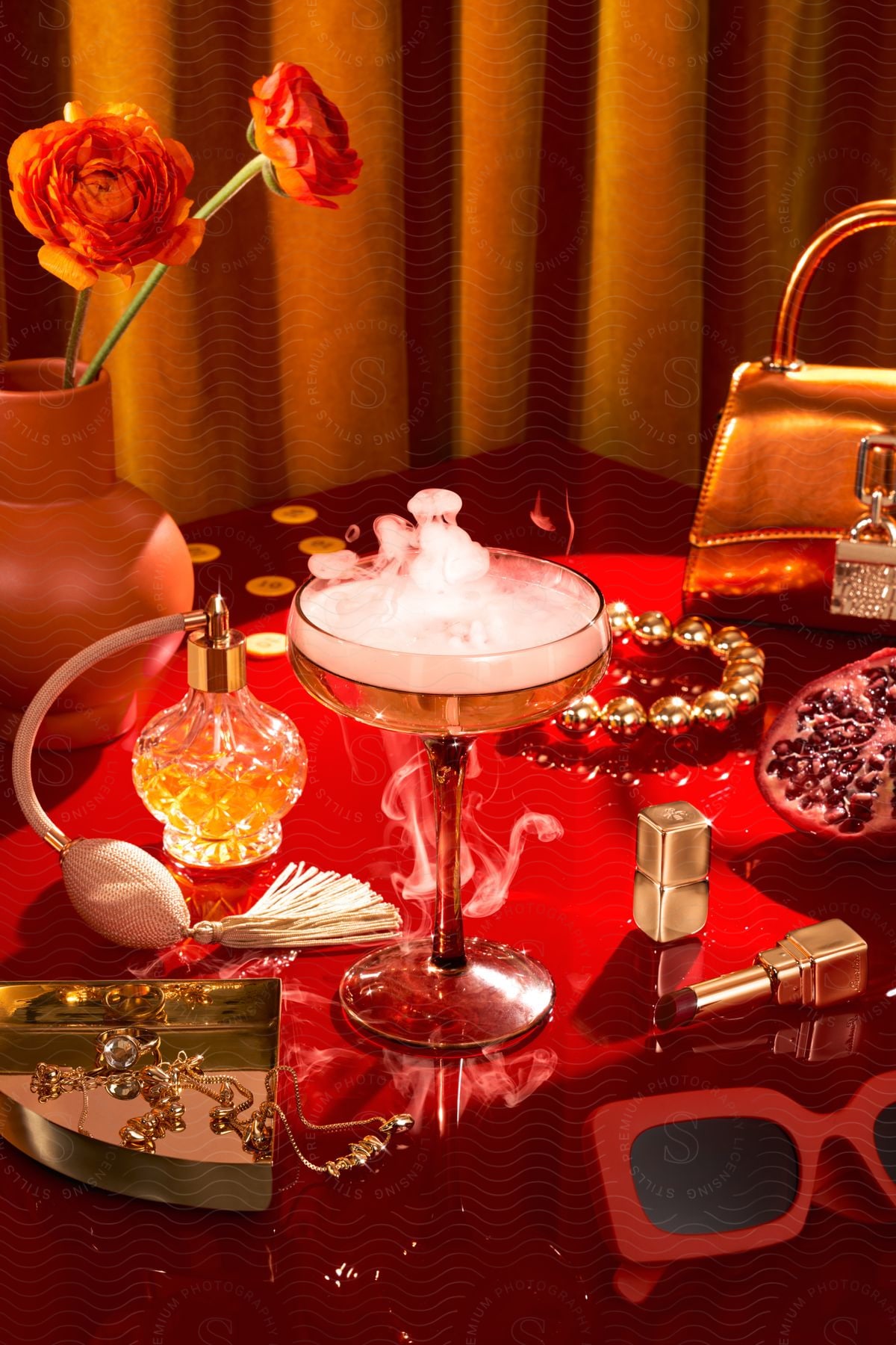 Table with beauty products and a drink in a crystal glass on a red table.