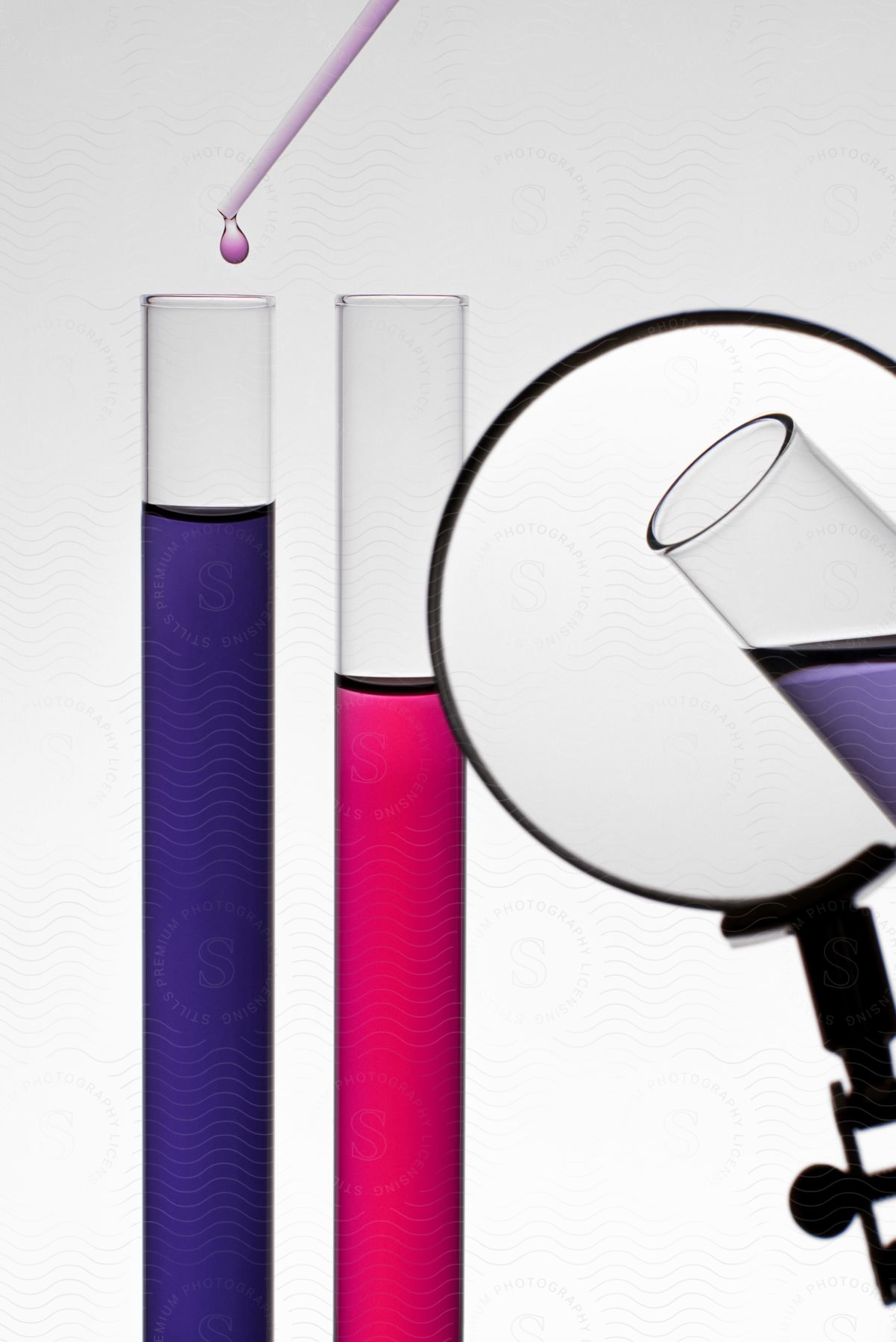 Dropper releasing pink liquid into test tube with magnifying glass focusing on empty test tube and two filled with purple and pink liquid against white background.