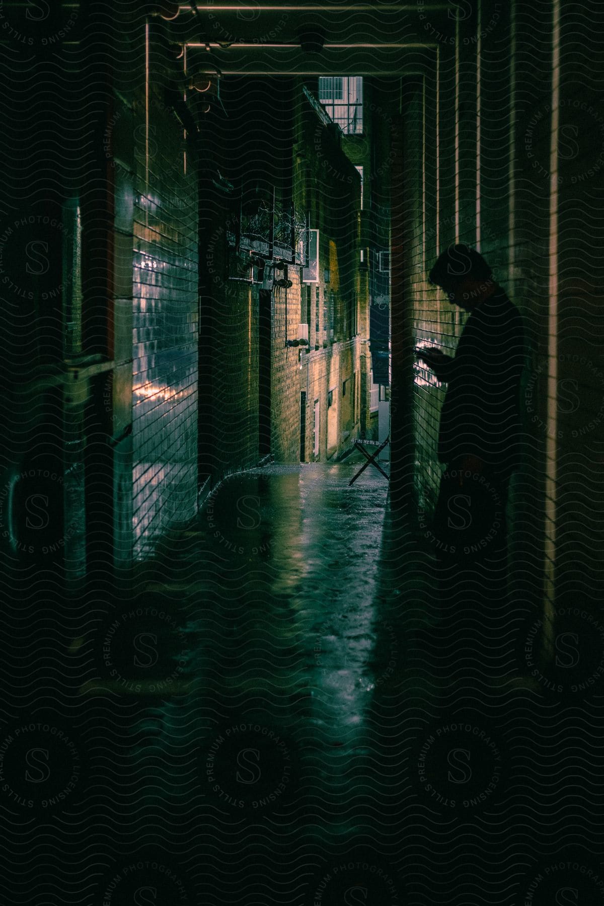 A man leaning against the wall in an alleyway, checking his phone