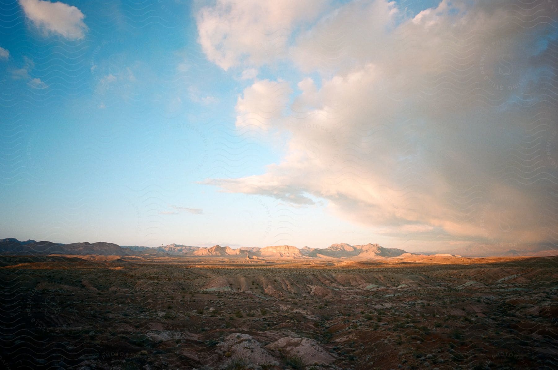 A vast arid landscape under a sky full of fluffy clouds during sunset.