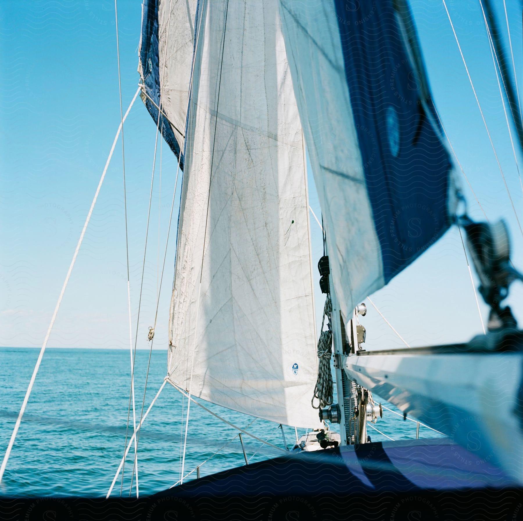 The white sail of a boat stands out in the foreground, with the clear blue ocean and sky in the background, creating a serene nautical scene.