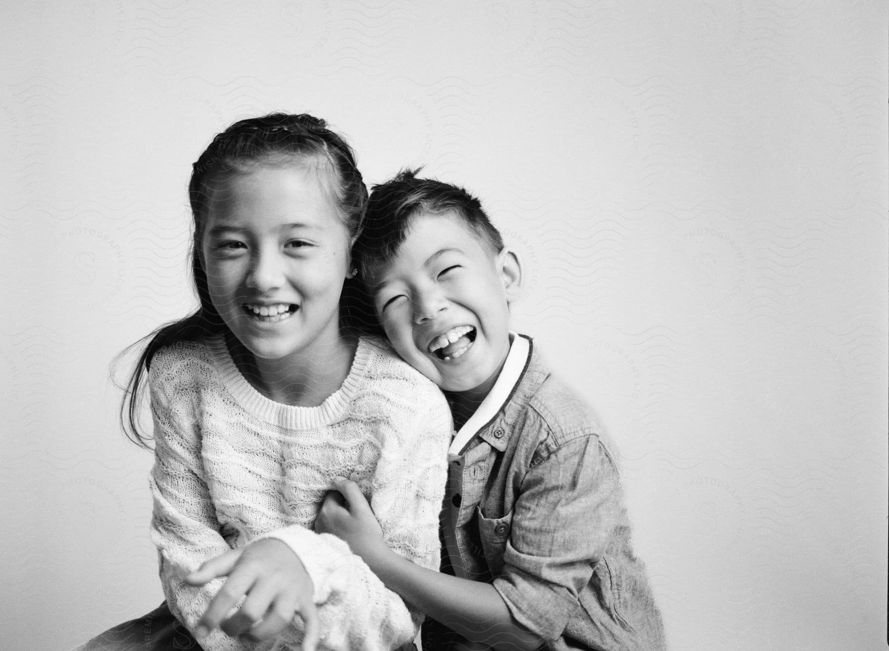 A boy holds a girl wearing a white knitwear, both smiling at the camera.