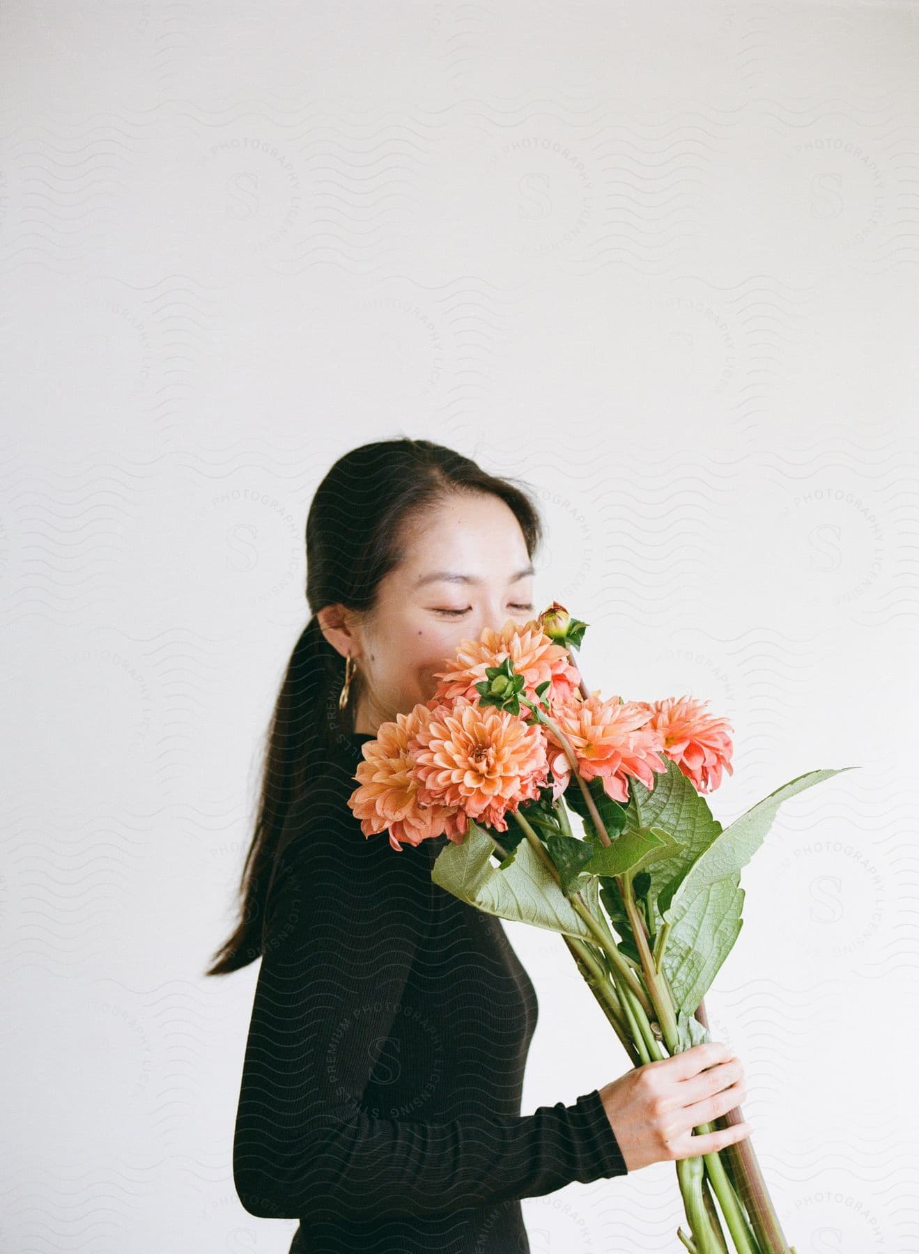 A young, Asian woman poses while smelling a bouquet of dahlia flowers.