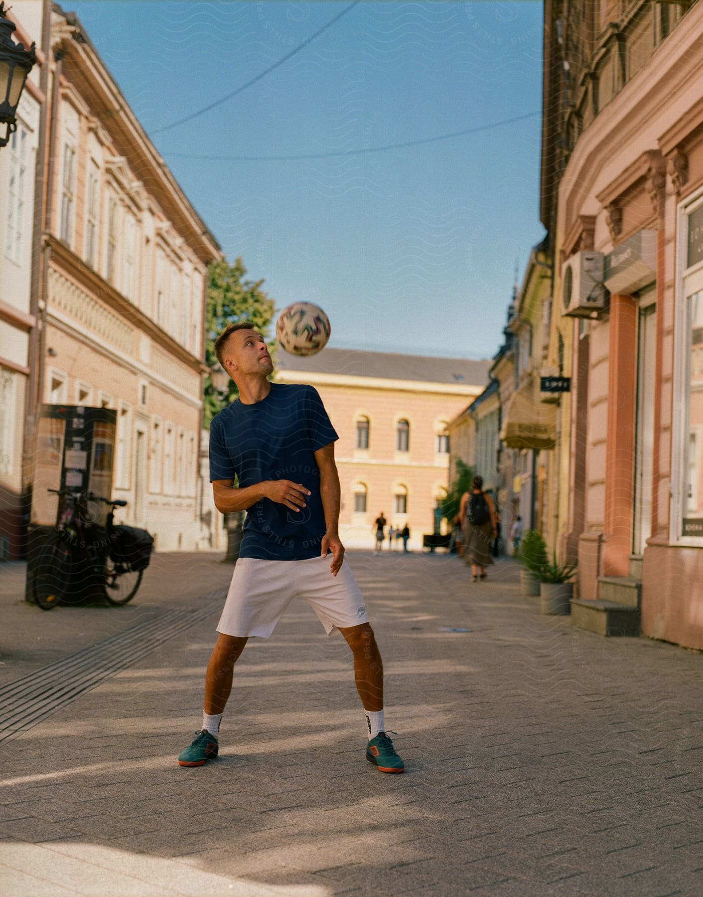 A young man playing with a soccer ball in the middle of a street.