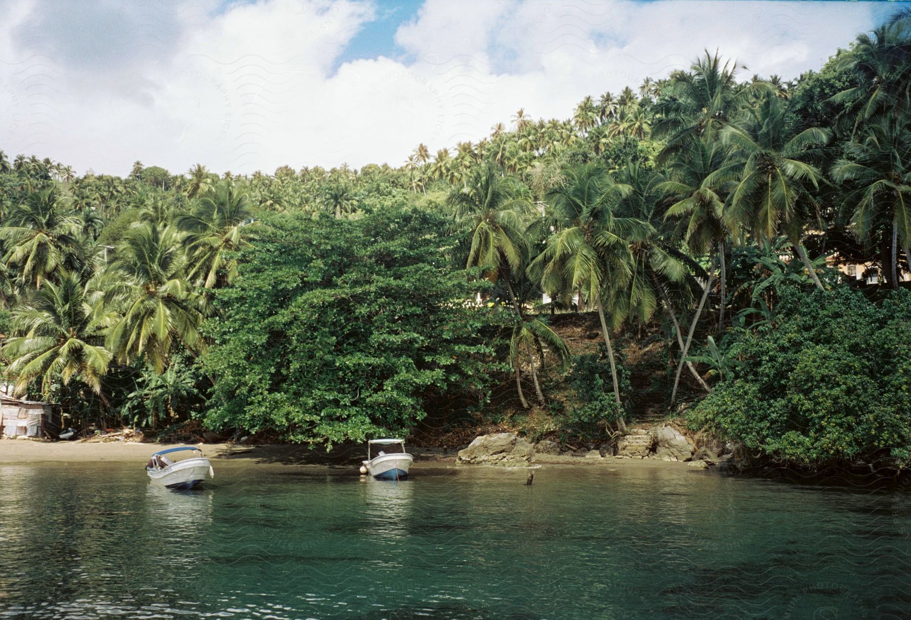 Two motor boats anchored near a beach and palm tree covered hill