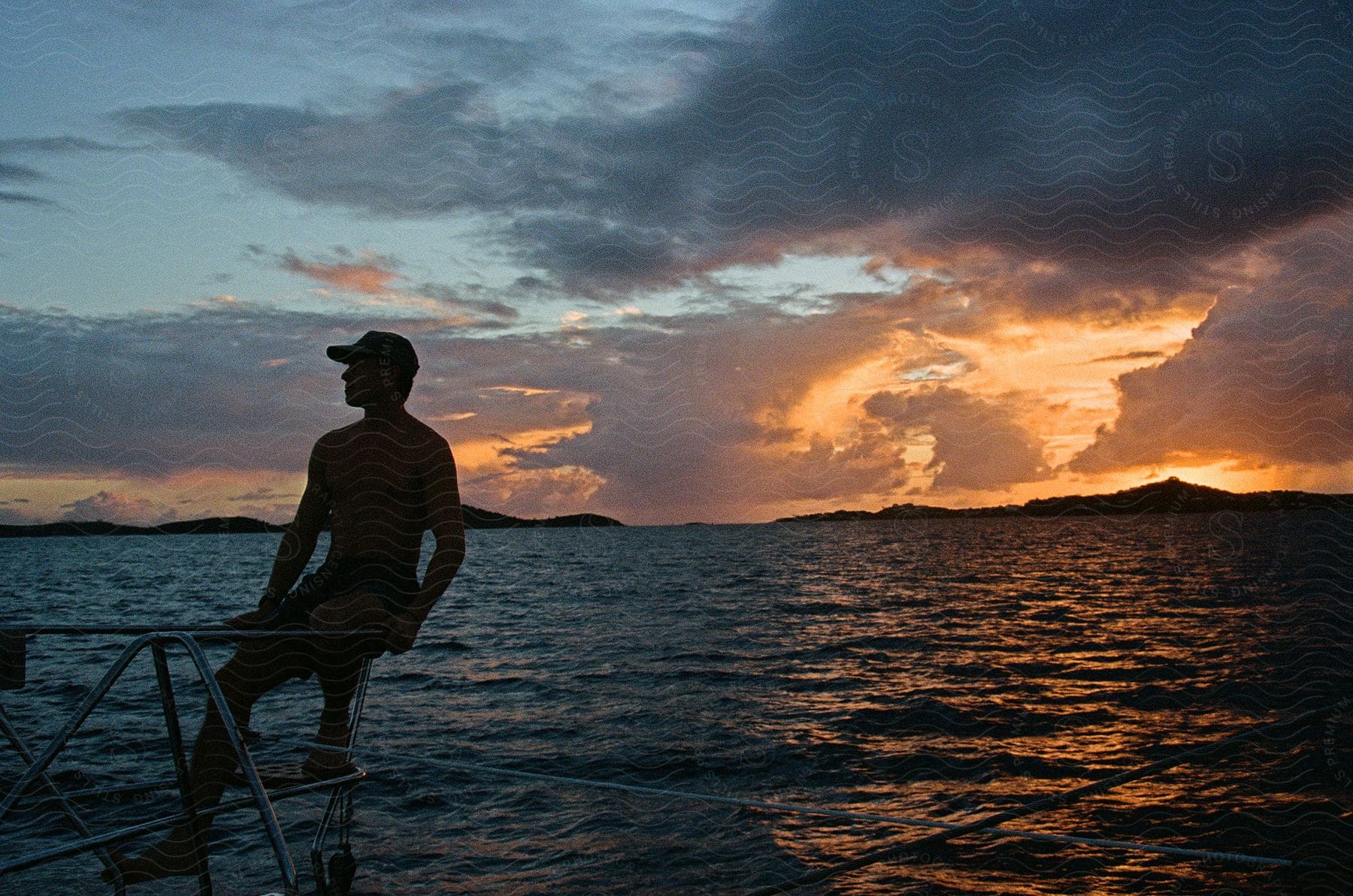 Man sitting along the coast as the sunset shines through the clouds and reflects on the water