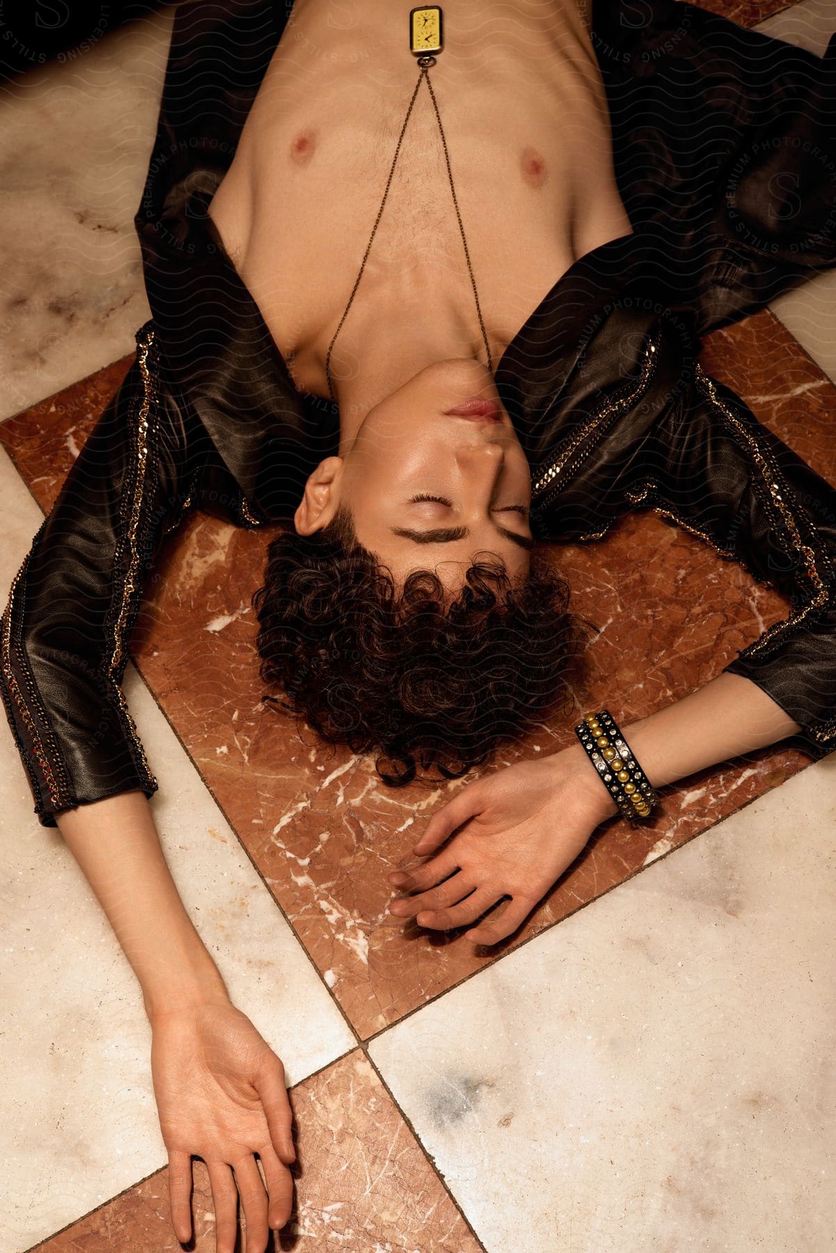 Young model lying on the floor in an open long-sleeved black shirt and wearing a necklace and bracelet.