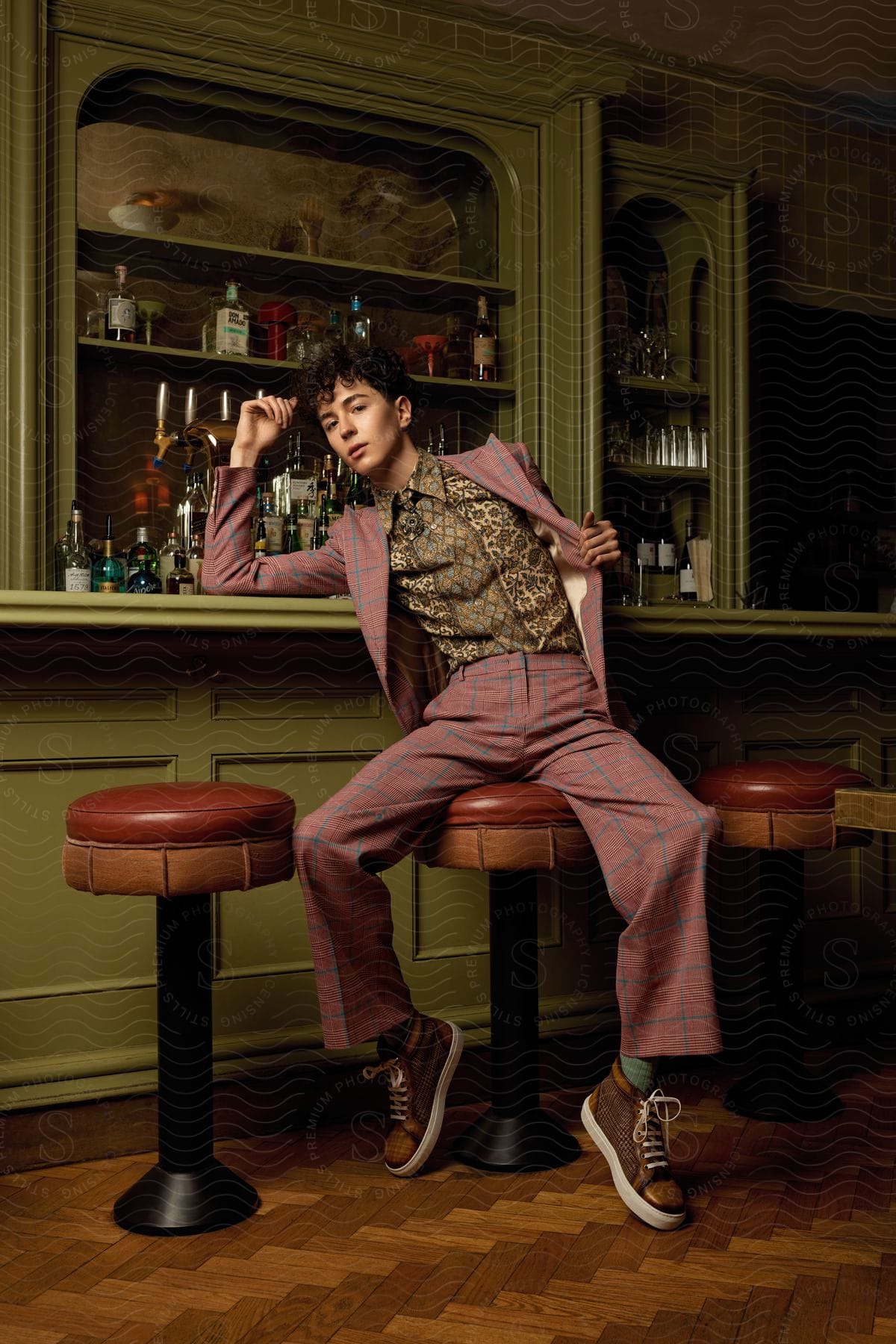 A young boy in pink clothes sits on a stool in a rustic bar