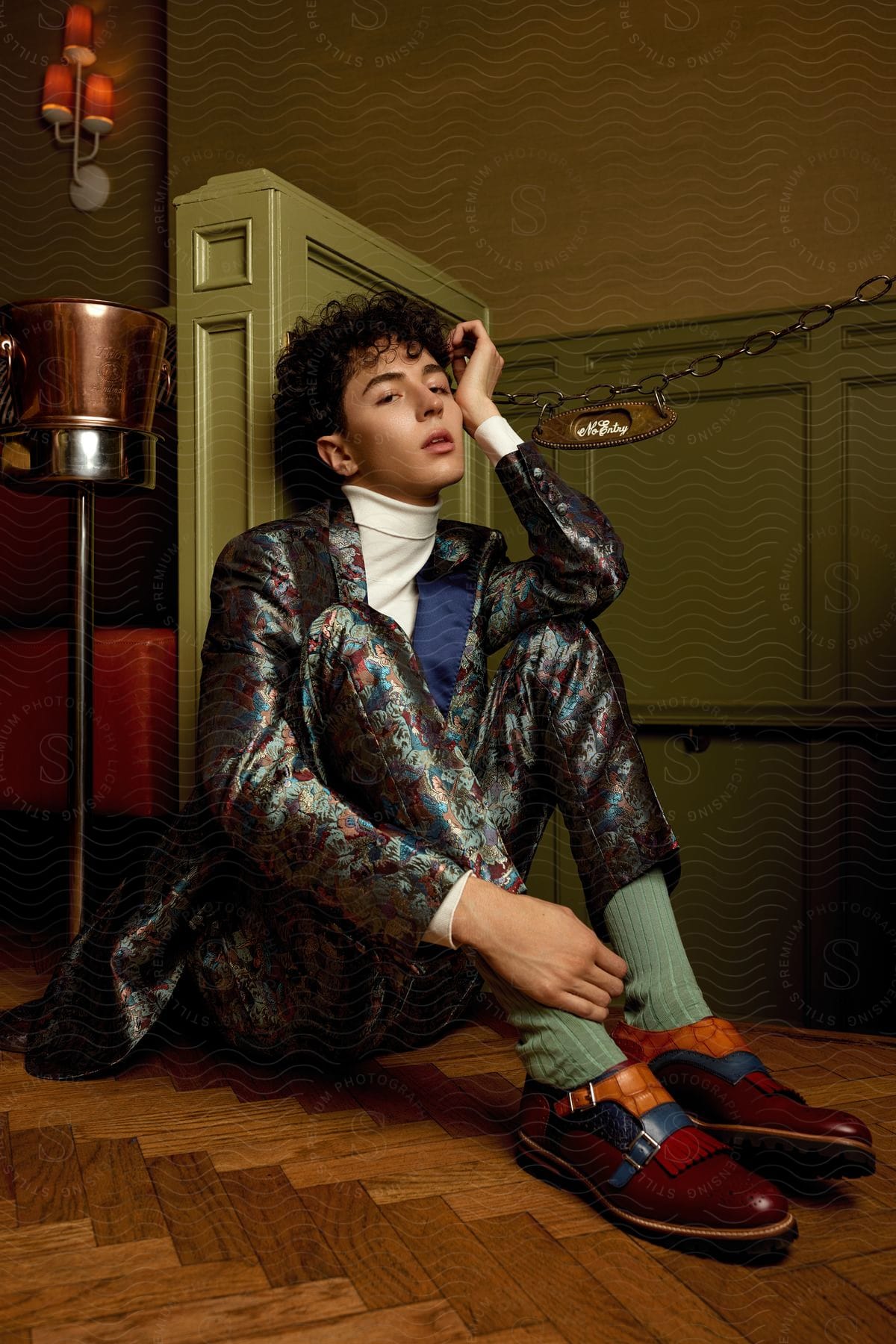 A young man is sitting on the floor wearing a gray formal outfit and dress shoes