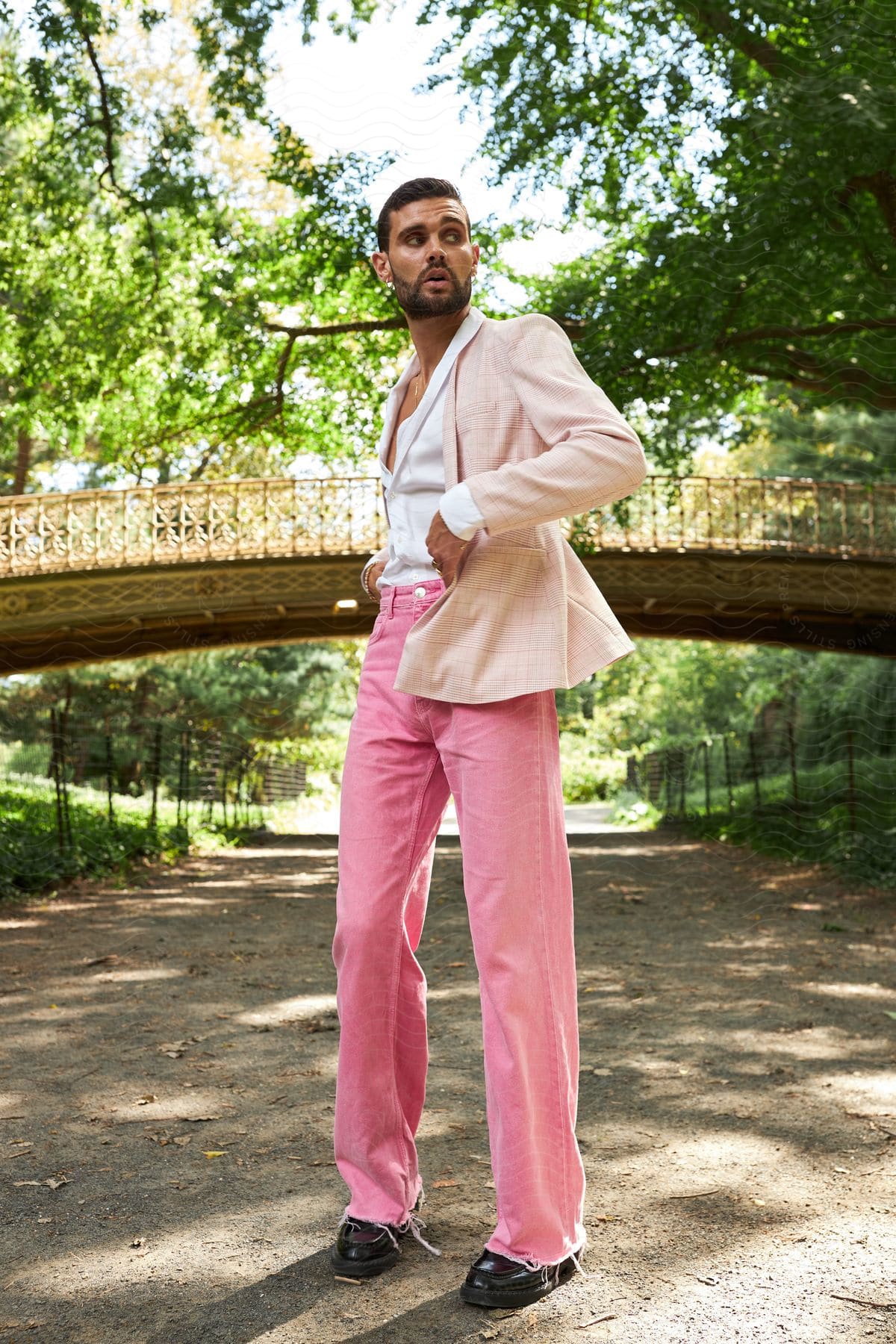 Model man posing in a blazer and pink pants in an outdoor setting with trees around him