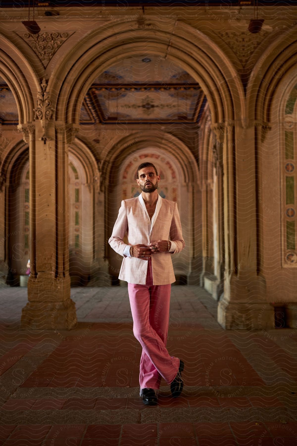 Model man posing indoors with ancient architecture and wearing a white shirt and pink pants with leather shoes