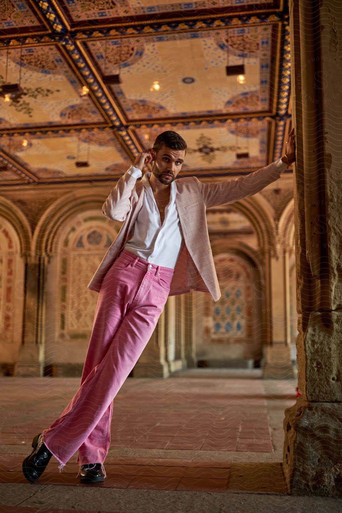 Man in pink trousers and white shirt with a beige jacket in a historic building with ornate ceiling.