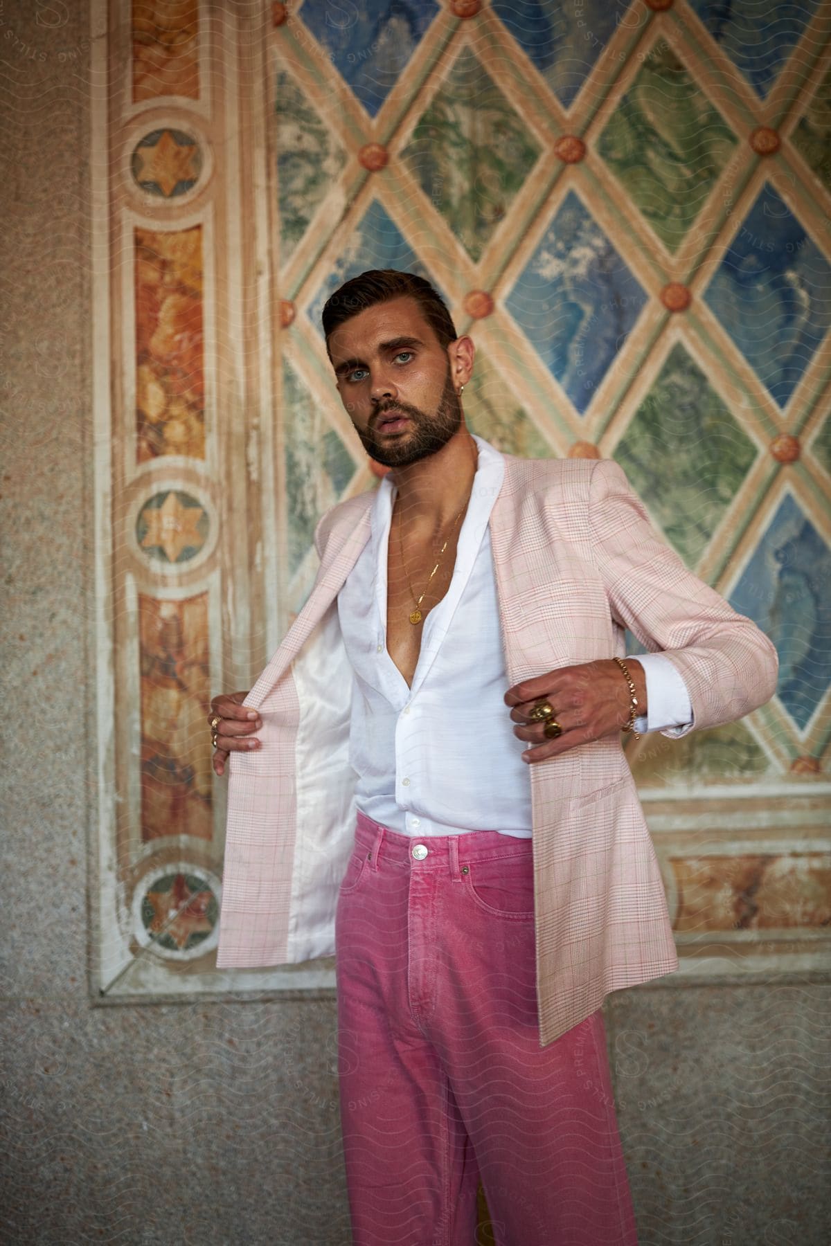 A man wearing a pink jacket standing near a rug on the wall