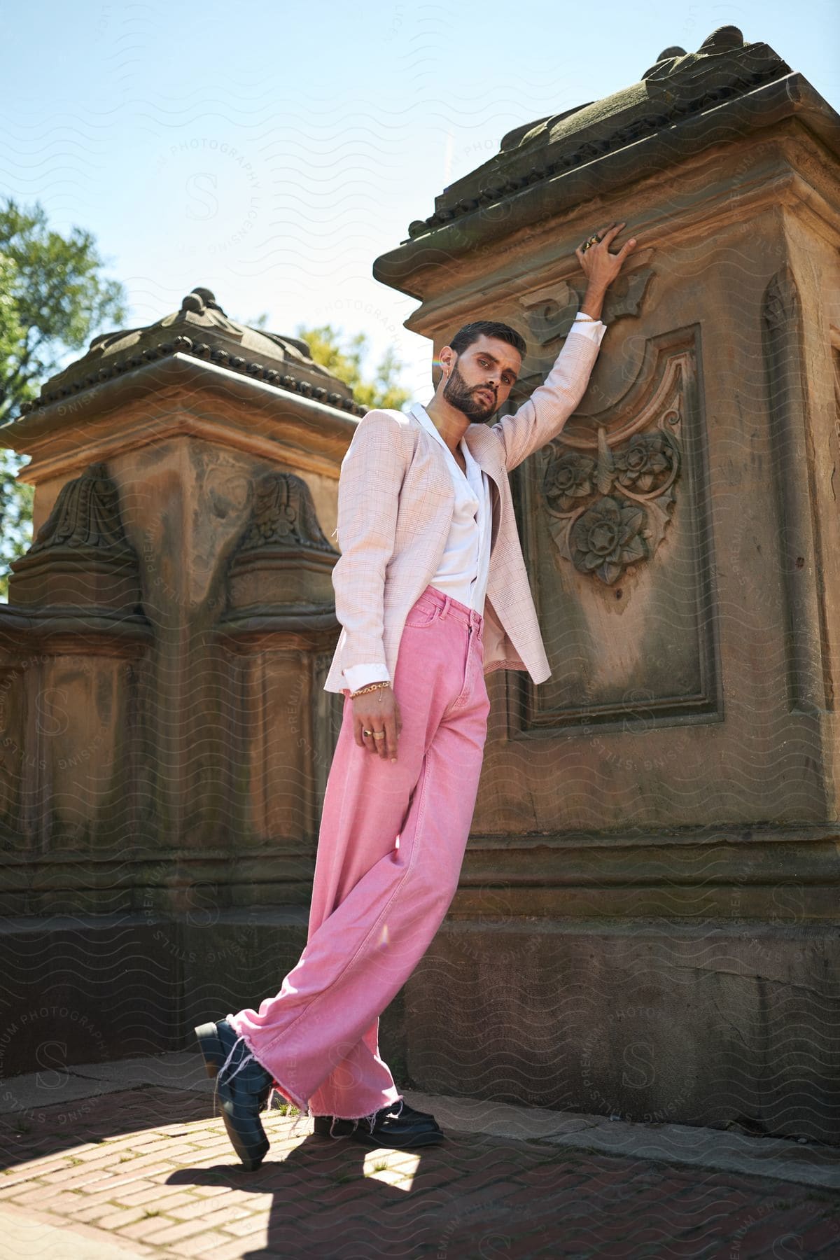 A man poses next to an ornate stone structure, wearing an elegant suit.