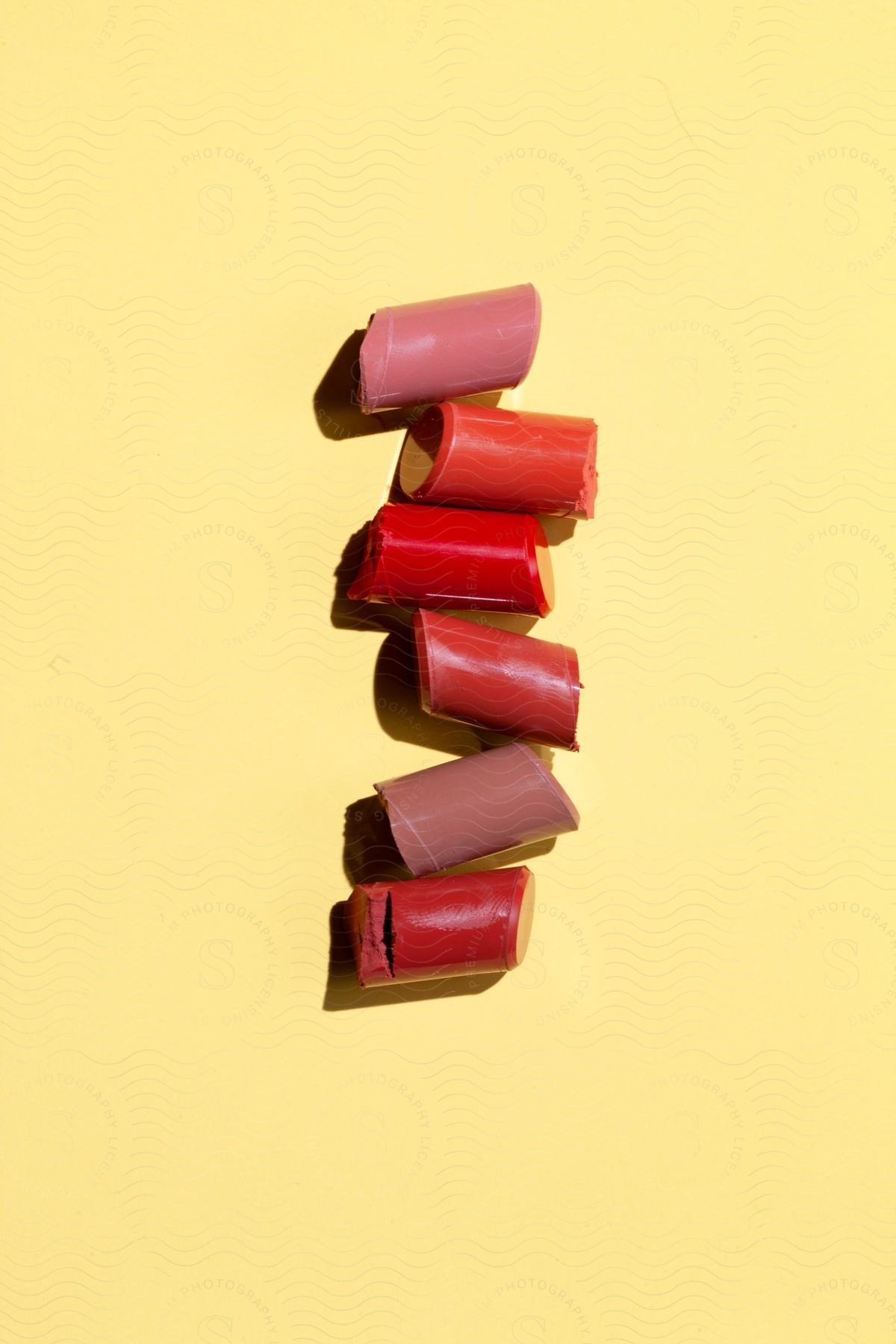 Pieces of broken lipstick, arranged on a bright yellow background. The lipsticks are in shades of red and pink, indicating a variety of colors.
