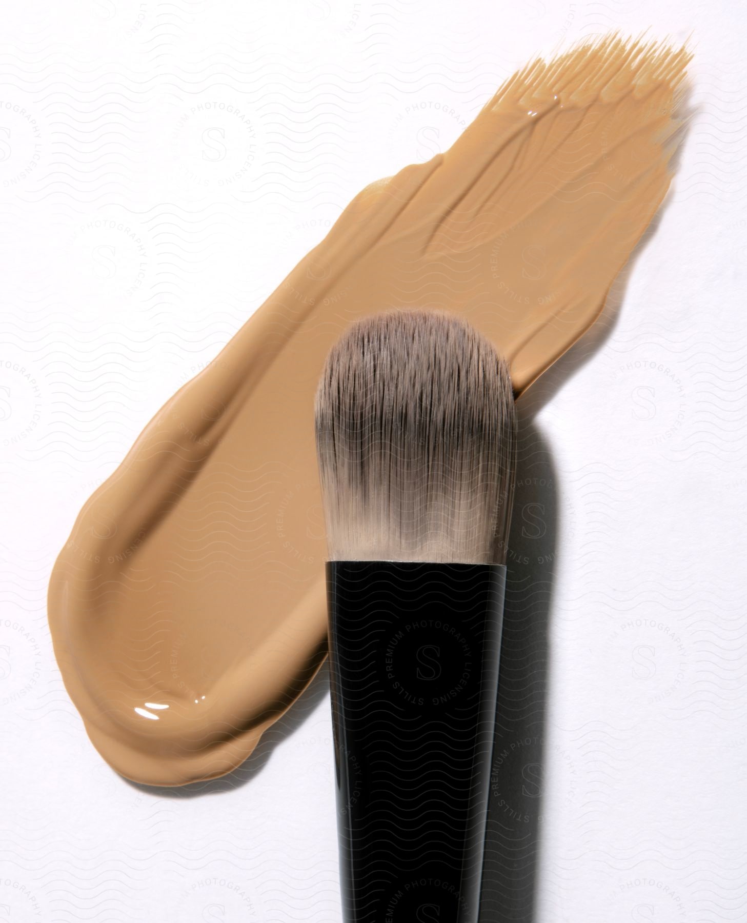 A makeup brush lies next to a streak of liquid foundation on a white surface.