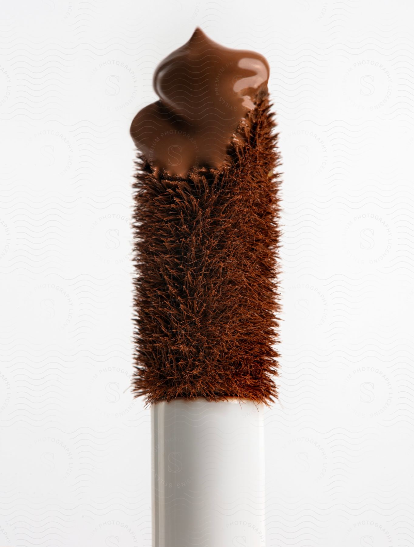 A close up of a brown make up brush with brown cream at the tip