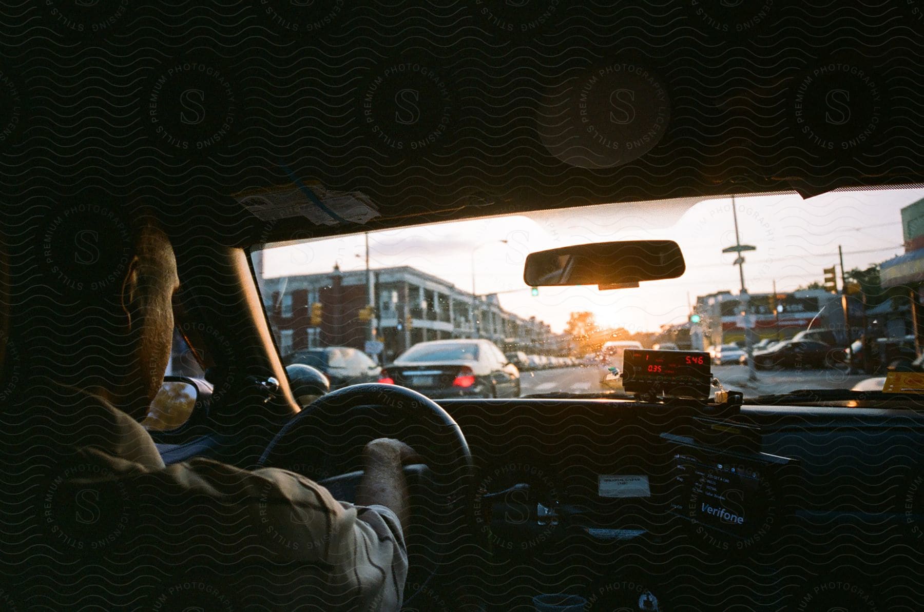 The interior of a car at sunset. The driver holds the steering wheel, and the golden light of the sun illuminates the room, creating a warm and cozy atmosphere.